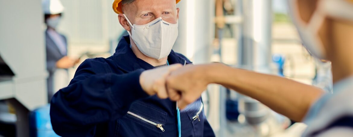Construction workers with face masks fist bumping during coronavirus epidemic.
